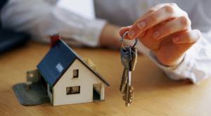 Persona sosteniendo un llavero con una maqueta de una casa pequeña al lado