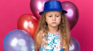 Niña con gorro de fiesta y globos detrás